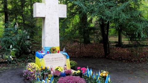 Steinernes Kreuz: Darunter ein mit Blumen und blaugelben Fahnen geschmücktes Grab.