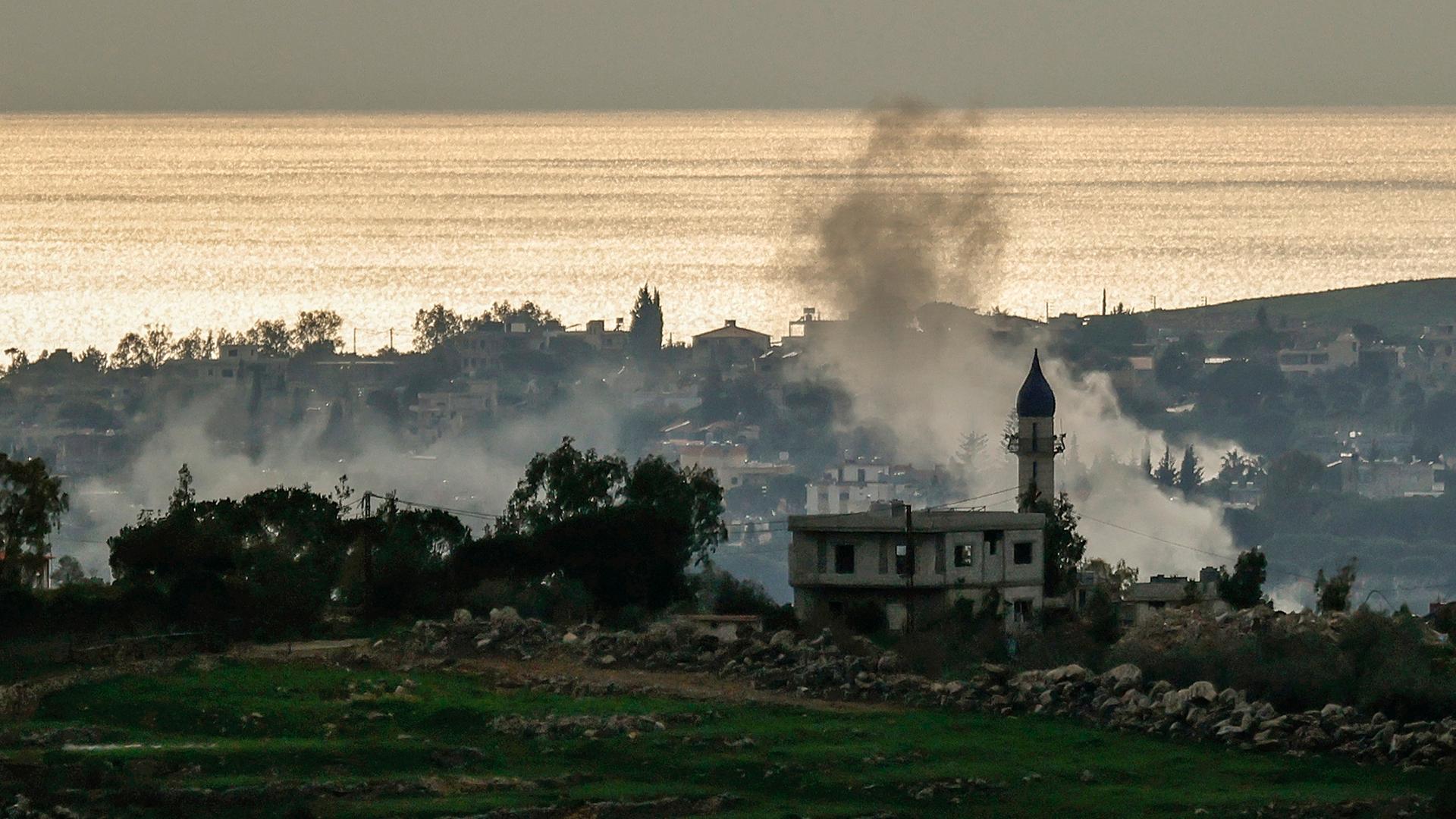 Aus einem Dorf nahe der Küste steigt Rauch auf.