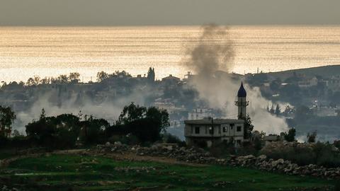 Aus einem Dorf nahe der Küste steigt Rauch auf.