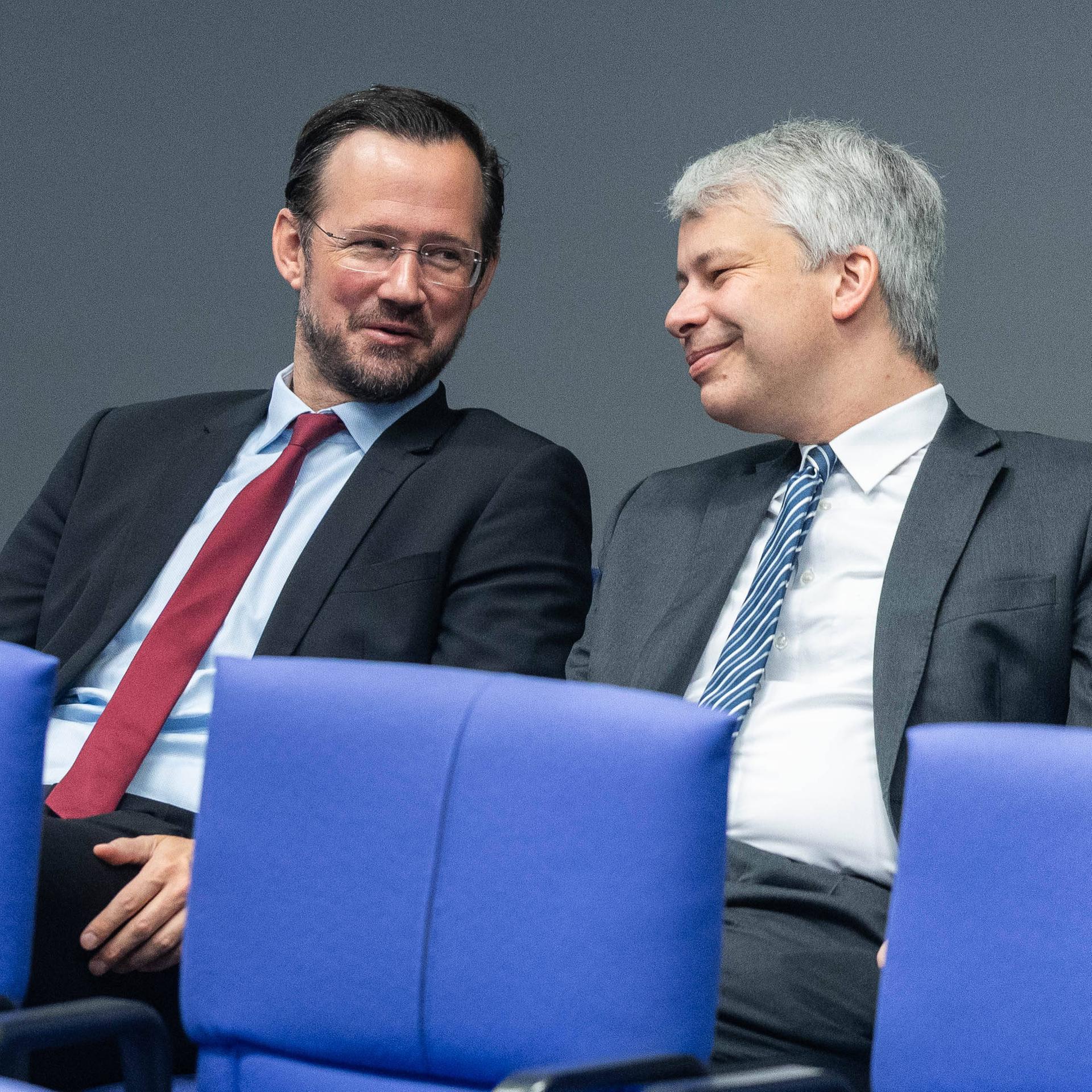 Die Politiker Dirk Wiese und Steffen Bilger sitzen auf blauen Stühlen im Bundestag nebeneinander.
