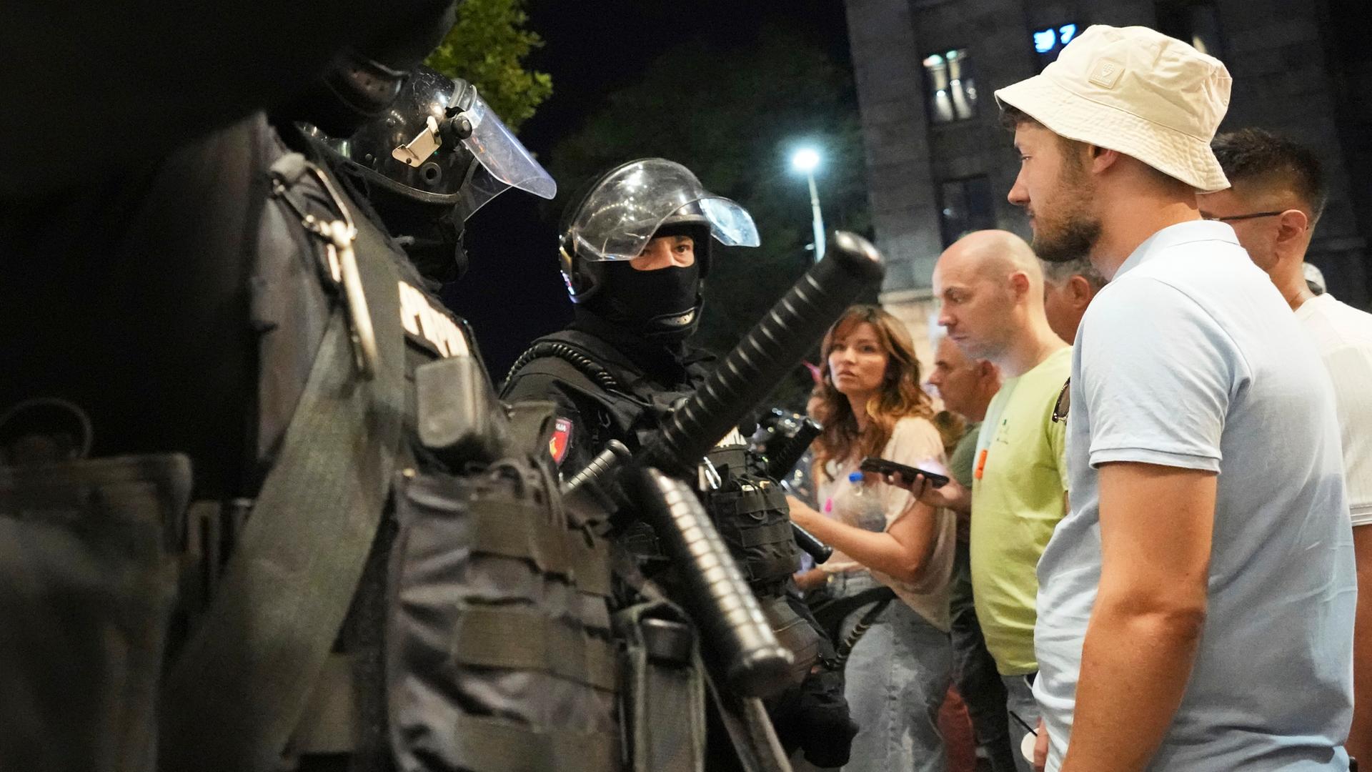 Die serbischen Sicherheitskräfte stehen in voller Montur unbewaffneten Zivilisten bei einem Protest gegenüber.  