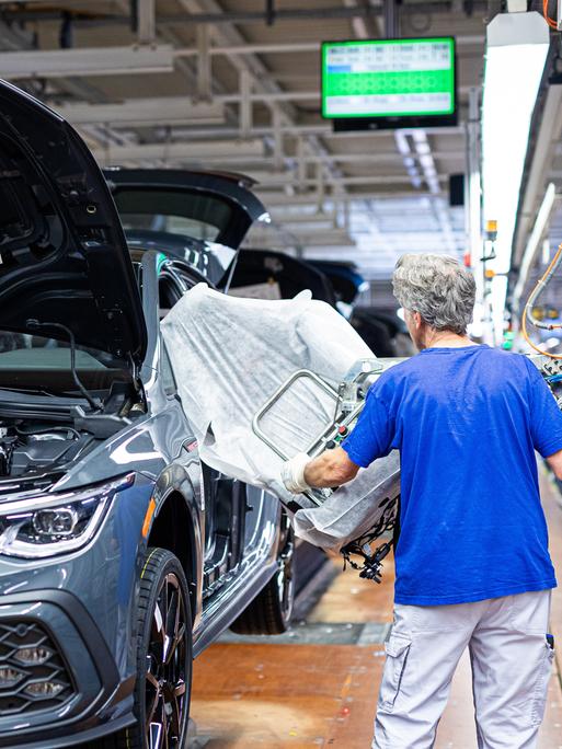 Ein Mitarbeiter montiert in einem Fahrzeug im VW Werk einen Autositz.