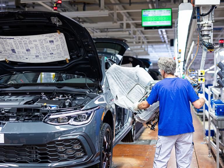 Ein Mitarbeiter montiert in einem Fahrzeug im VW Werk einen Autositz.