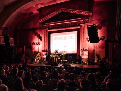 Blick auf die Bühne von UT Connewitz, auf der ein Konzert der Leipziger Jazztage stattfindet, das mit einem großen Aufhänger auf der Bühne kenntlich gemacht ist.