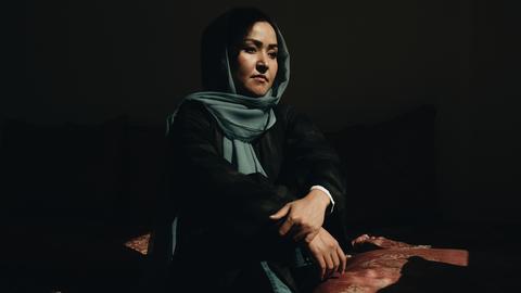 Ein Frau mit Kopftuch sitzt auf einem Sitzkissen.