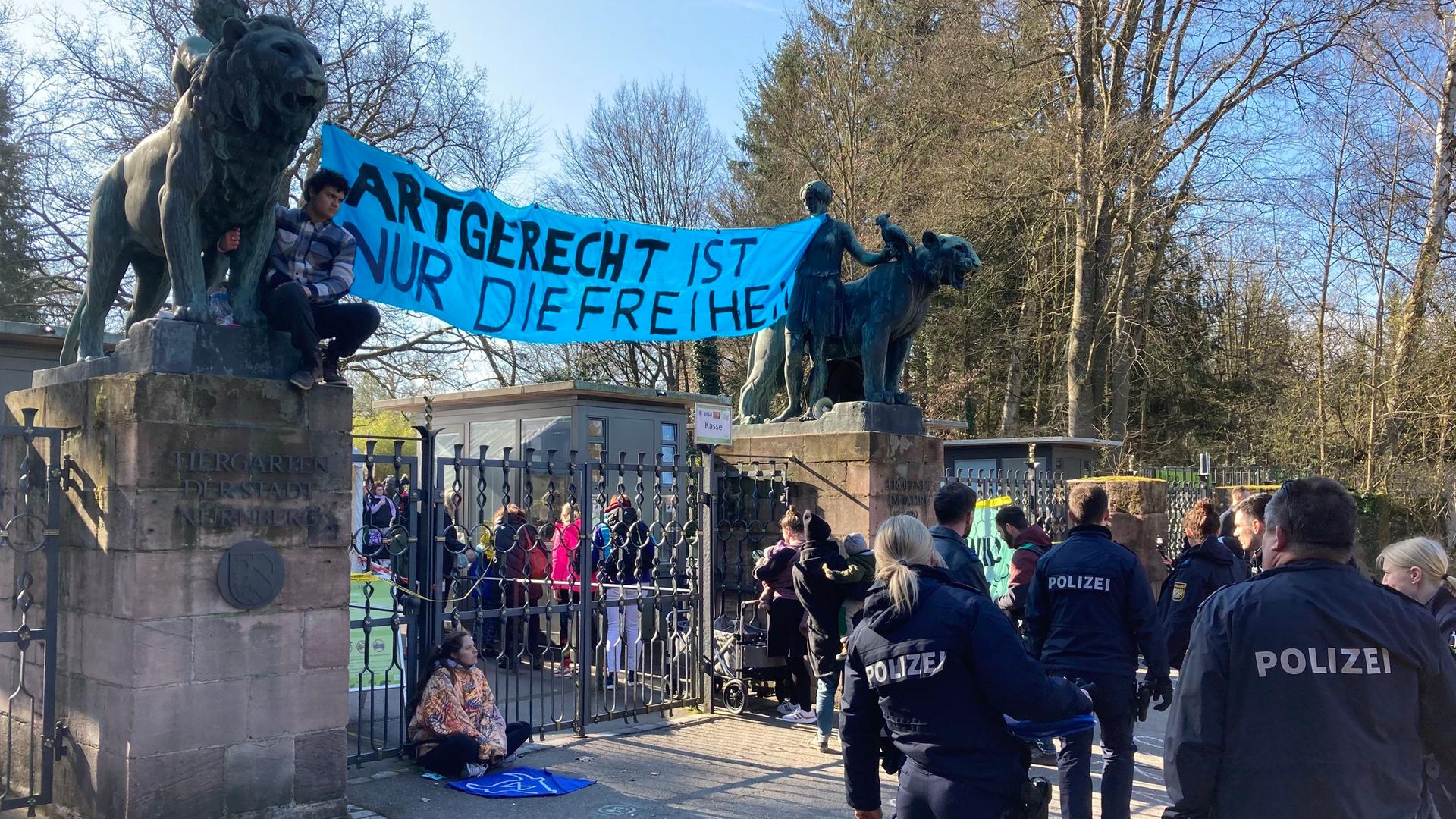 Die Aktivisten halten ein Banner mit der Aufschrift "Artgerecht ist nur die Freiheit" hoch. Polizisten beobachten Tierschutzaktivisten, die den Eingang des Nürnberger Tierparks blockieren.
