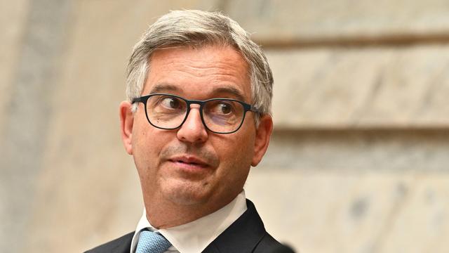 Porträtaufnahme Brunners während einer Pressekonferenz. Er schaut ernst an der Kamera vorbei. 
