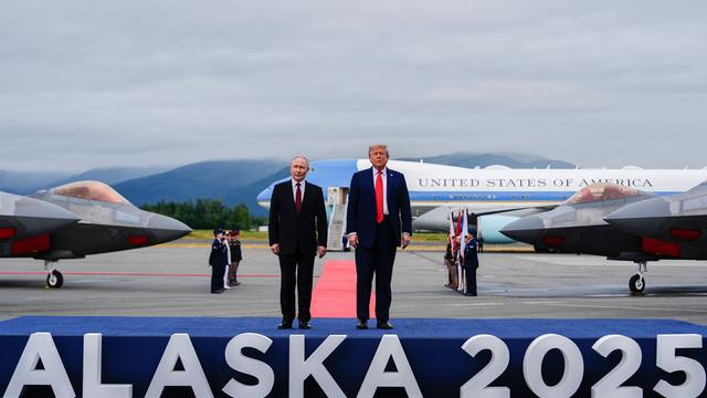 US-Präsident Donald Trump und der russische Präsident Wladimir Putin stehen auf einem Flughafen auf einem Podest, auf dem "Alaska 2025" steht.