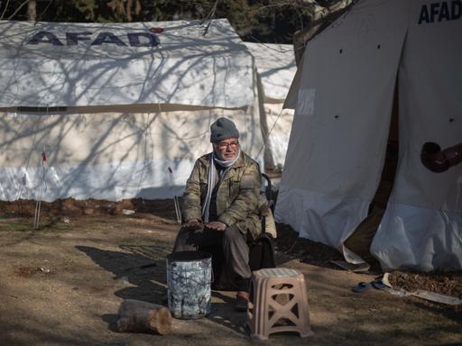 Türkei, Kahramanmaras: Ein Mann sitzt vor seinem Zelt und wärmt sich in einem Behelfslager für Menschen, die ihre Häuser im Epizentrum des Erdbebens verloren haben.
