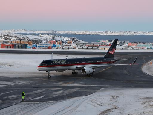 Ein Flugzeug mit dem Schriftzug "Trump" darauf steht auf einer Landebahn, auf der Schnee liegt. Dahinter ist eine Ansammlung von Häusern zu sehen.