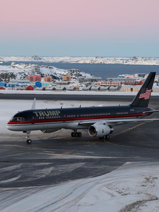 Ein Flugzeug mit dem Schriftzug "Trump" darauf steht auf einer Landebahn, auf der Schnee liegt. Dahinter ist eine Ansammlung von Häusern zu sehen.