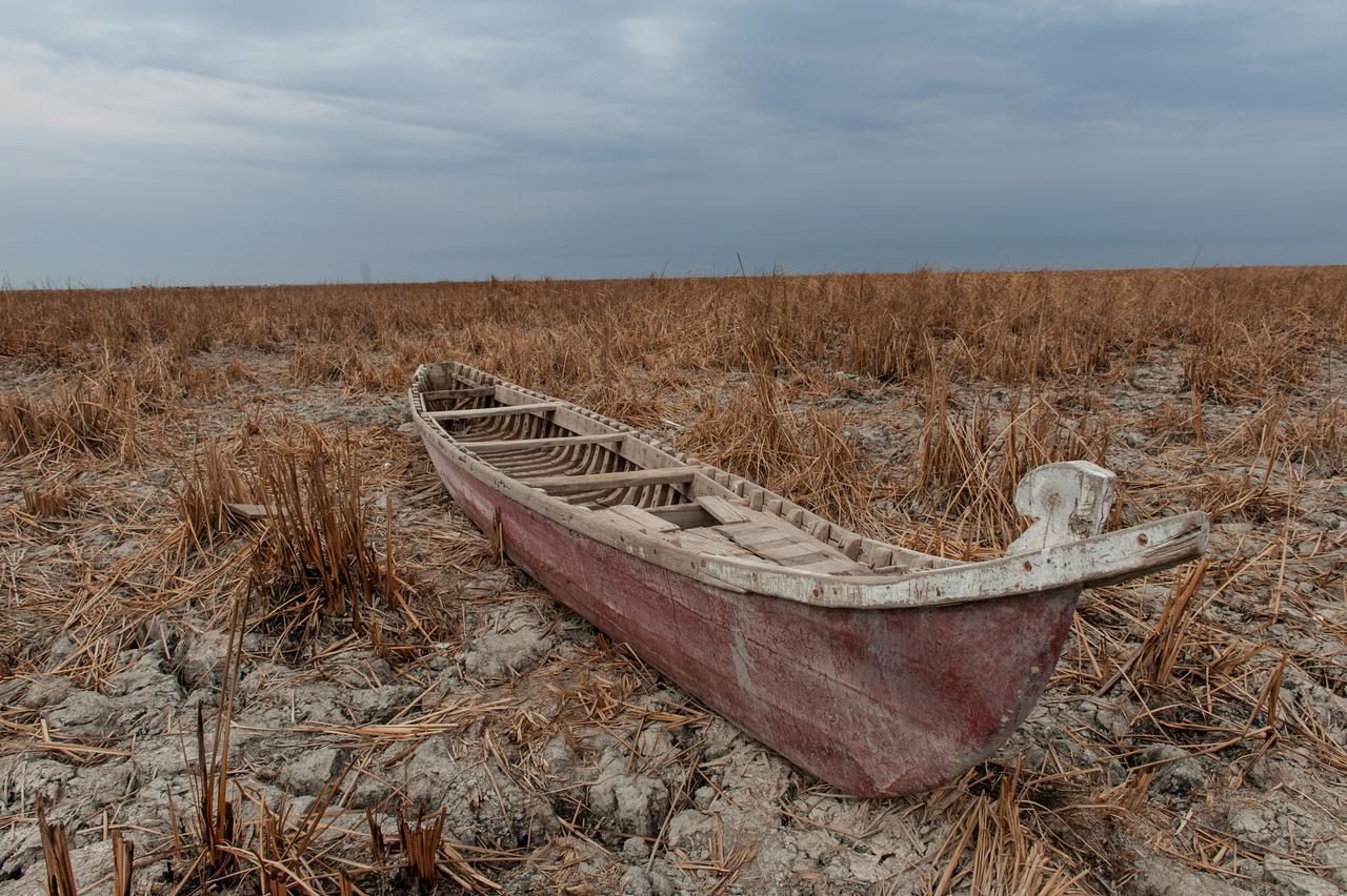 Ein rötliches Boot liegt in einer trockenen Wüstenlandschaft. Wasser ist weit und breit keines zu sehen.