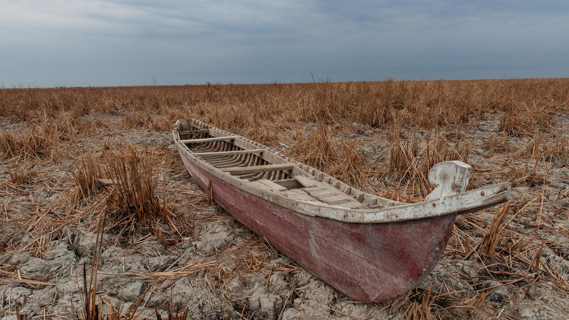 Ein rötliches Boot liegt in einer trockenen Wüstenlandschaft. Wasser ist weit und breit keines zu sehen.