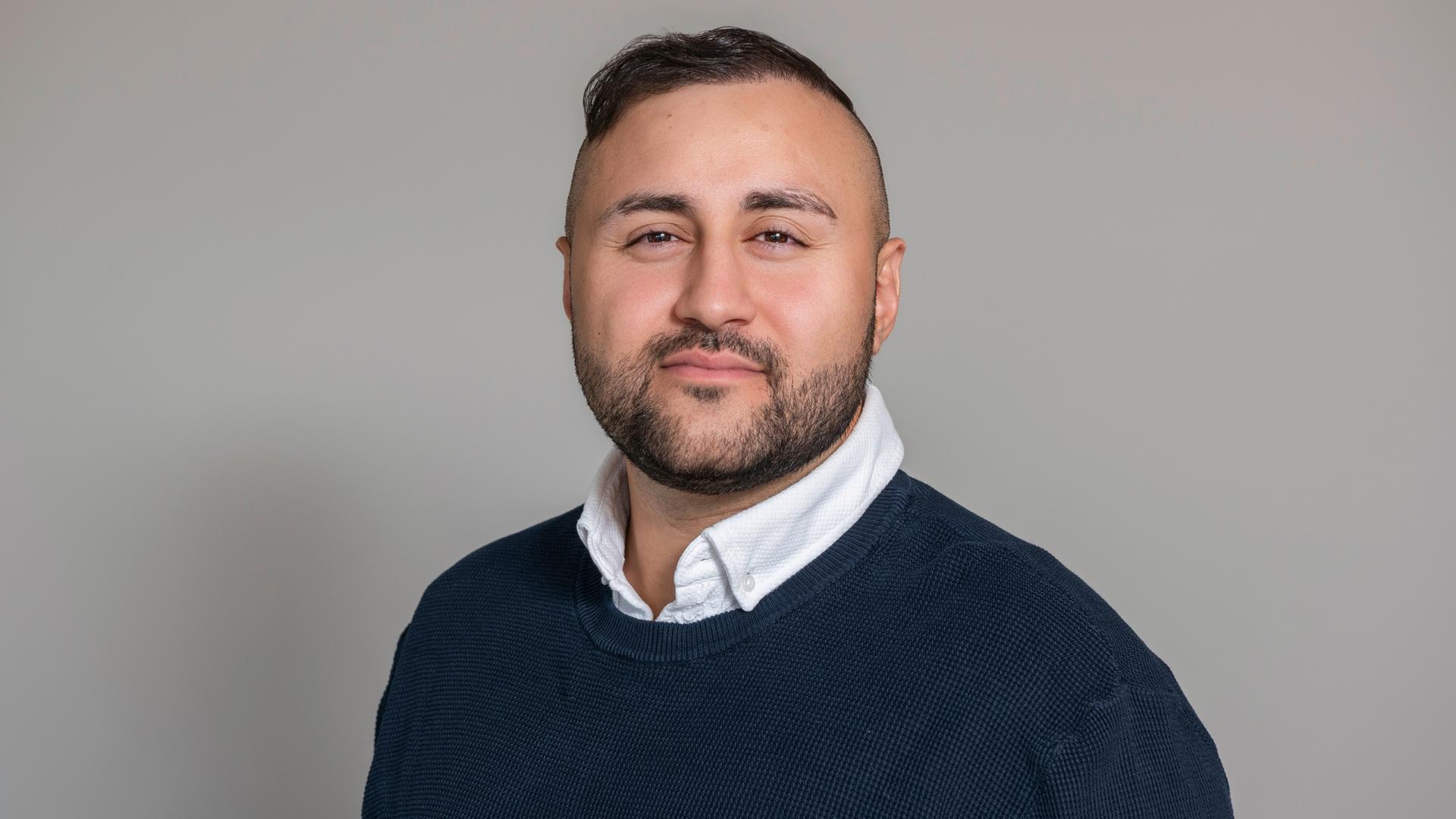 Porträt des Arztes und Autors Dr. Mahmut Martin Yüksel. Er trägt einen blauen Pullover, am Hals schaut ein weißer Hemdkragen hervor. Er blickt selbstbewusst in die Kamera. Porträt des Arztes und Autors Dr. Mahmut Martin Yüksel. Er trägt einen blauen Pullover, am Hals schaut ein weißer Hemdkragen hervor. Er blickt selbstbewusst in die Kamera.