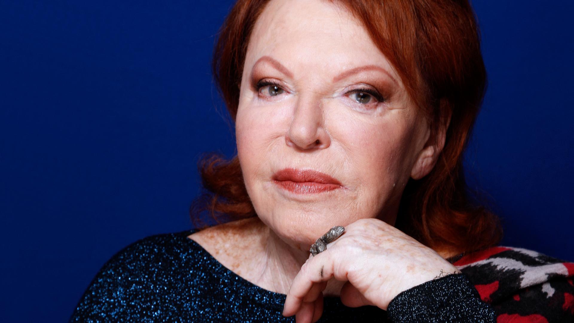 Eine ältere Frau mit rot gefärbten Haaren blickt ernst in die Kamera.