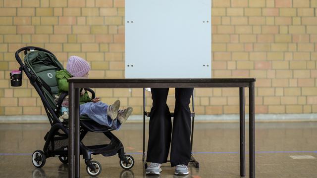 Eine Frau steht in einer Turnhalle in Duisburg in einer Wahl-Kabine. Neben ihr steht ein Kinder-Wagen mit einem Kind. 