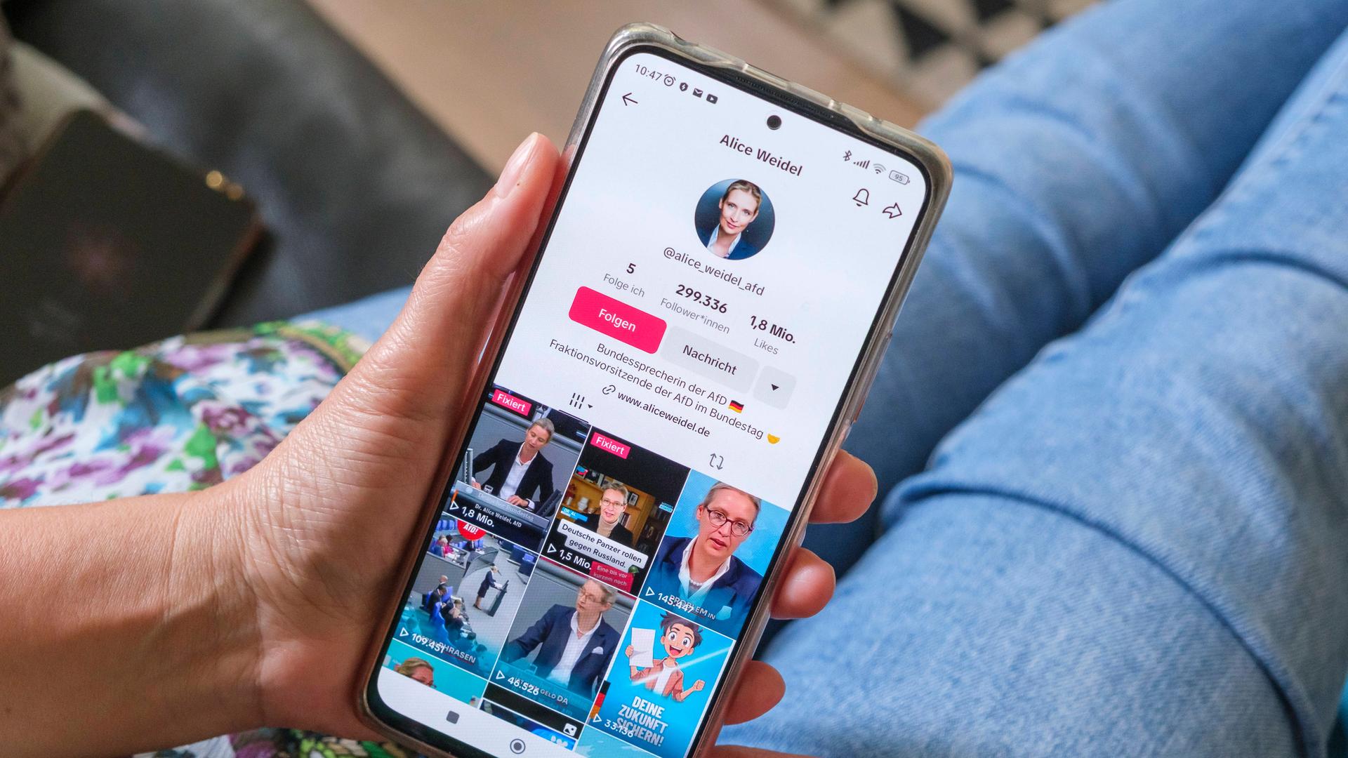 Frau hält ein Mobiltelefon auf dessen Display die Seite der AFD Politikerin Alice Weidel auf Plattform TikTok zu sehen ist.