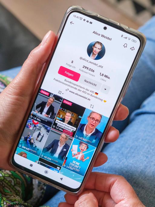 Frau hält ein Mobiltelefon auf dessen Display die Seite der AFD Politikerin Alice Weidel auf Plattform TikTok zu sehen ist.