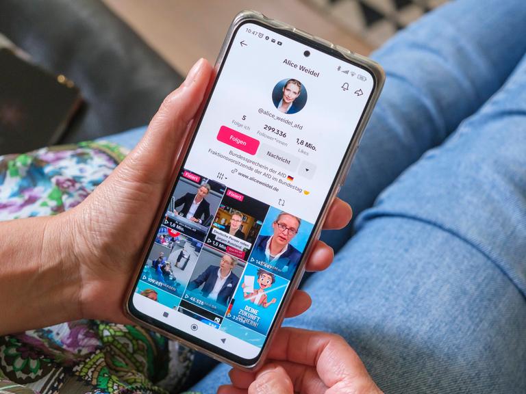 Frau hält ein Mobiltelefon auf dessen Display die Seite der AFD Politikerin Alice Weidel auf Plattform TikTok zu sehen ist.