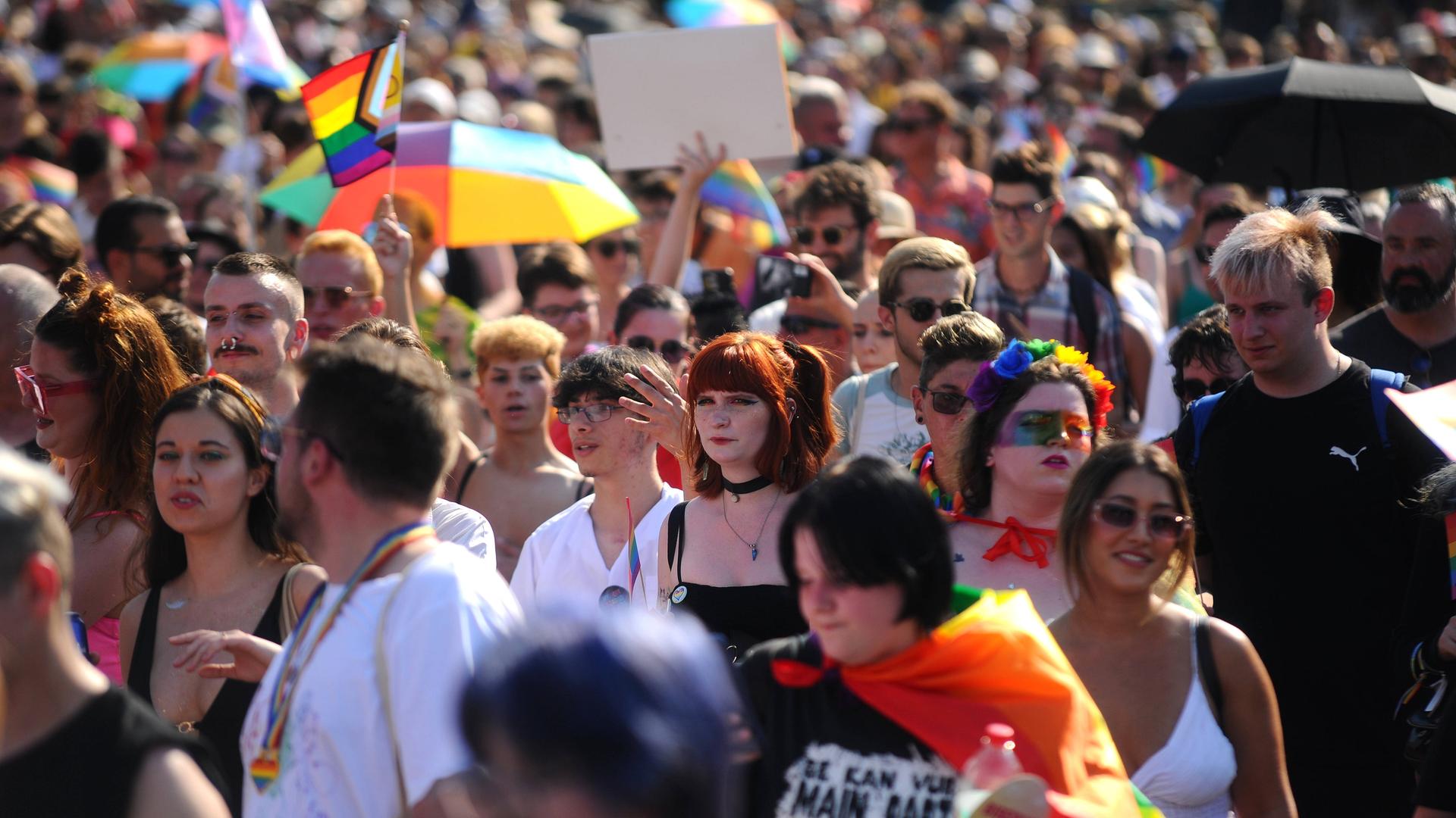 Viele Menschen laufen während der Pride-Parade 2023 in Budapest auf der Straße und halten teils Plakate und bunte Flaggen hoch.