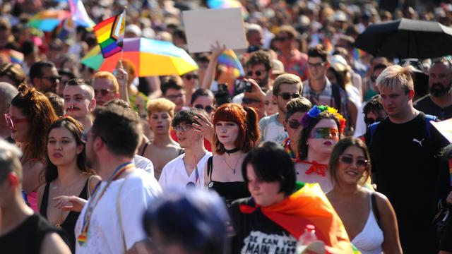 Viele Menschen laufen während der Pride-Parade 2023 in Budapest auf der Straße und halten teils Plakate und bunte Flaggen hoch.