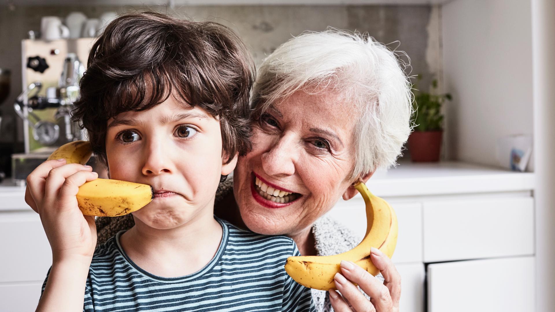 Eine gut gelaunte ältere Dame und ein Junge halten sich Bananen an die Ohren, so als wären es Telefone. Eine gut gelaunte ältere Dame und ein Junge halten sich Bananen an die Ohren, so als wären es Telefone.