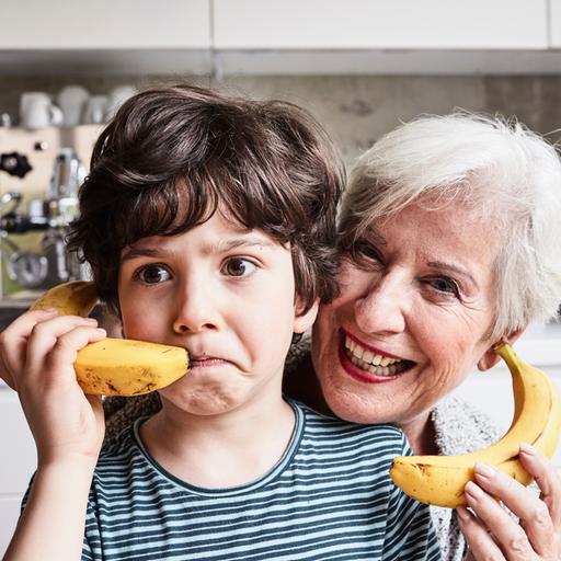 Eine gut gelaunte ältere Dame und ein Junge halten sich Bananen an die Ohren, so als wären es Telefone. 