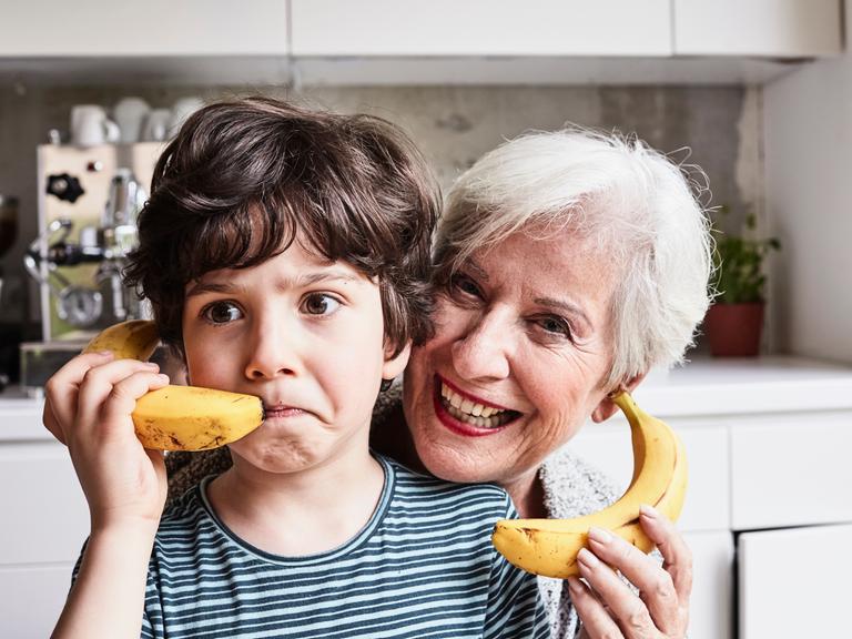 Eine gut gelaunte ältere Dame und ein Junge halten sich Bananen an die Ohren, so als wären es Telefone. 