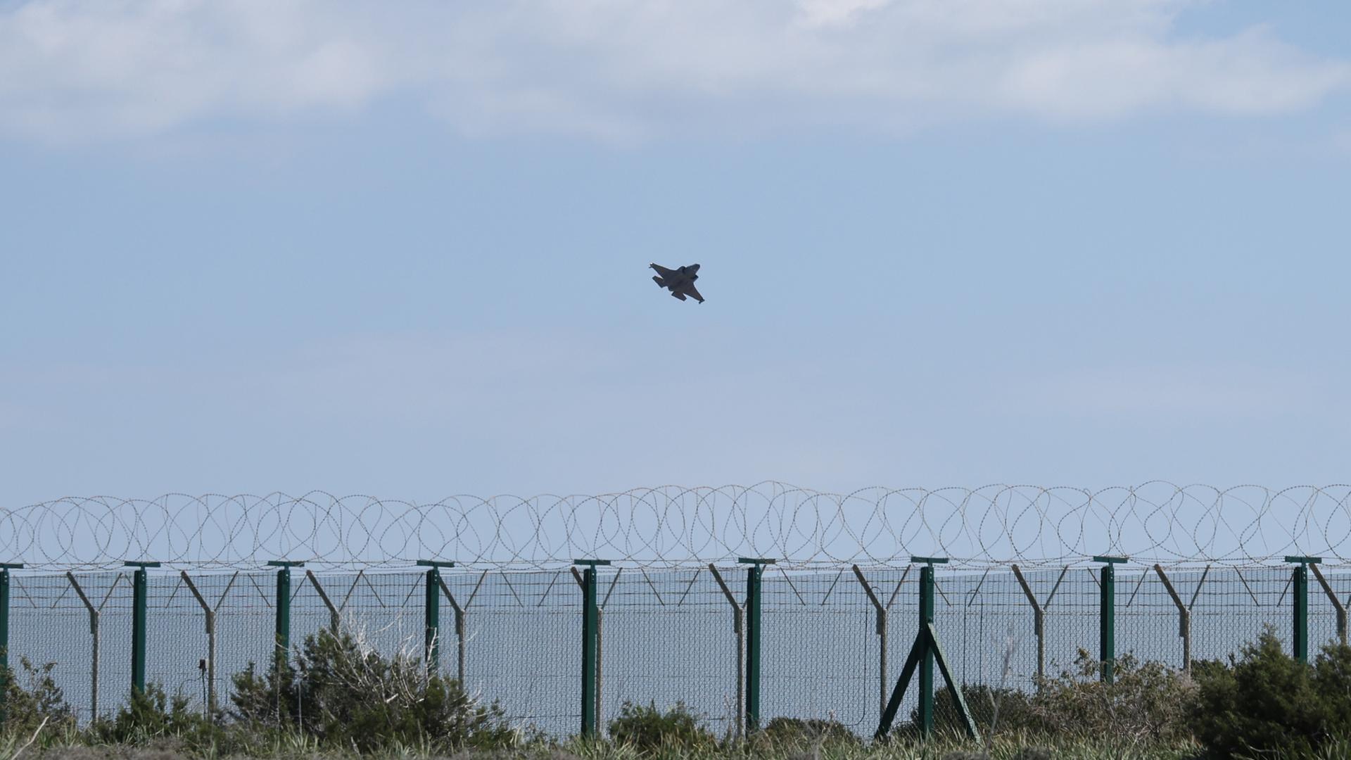Ein Militärflugzeug startet über dem Meer von Zypern. Im Vordergrund steht ein Zaun mit NATO-Draht. Ein Militärflugzeug startet über dem Meer von Zypern. Im Vordergrund steht ein Zaun mit NATO-Draht.