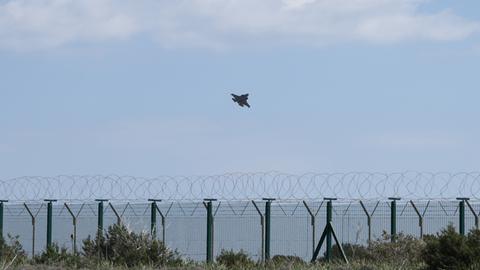 Ein Militärflugzeug startet über dem Meer von Zypern. Im Vordergrund steht ein Zaun mit NATO-Draht. Ein Militärflugzeug startet über dem Meer von Zypern. Im Vordergrund steht ein Zaun mit NATO-Draht.