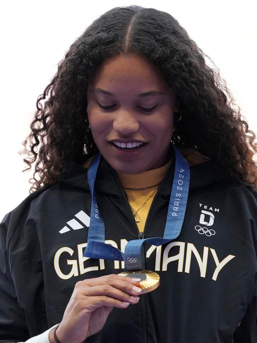 Ogunleye steht auf dem Podium und sieht sich ihre Goldmedaille an.