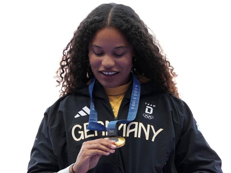 Ogunleye steht auf dem Podium und sieht sich ihre Goldmedaille an.