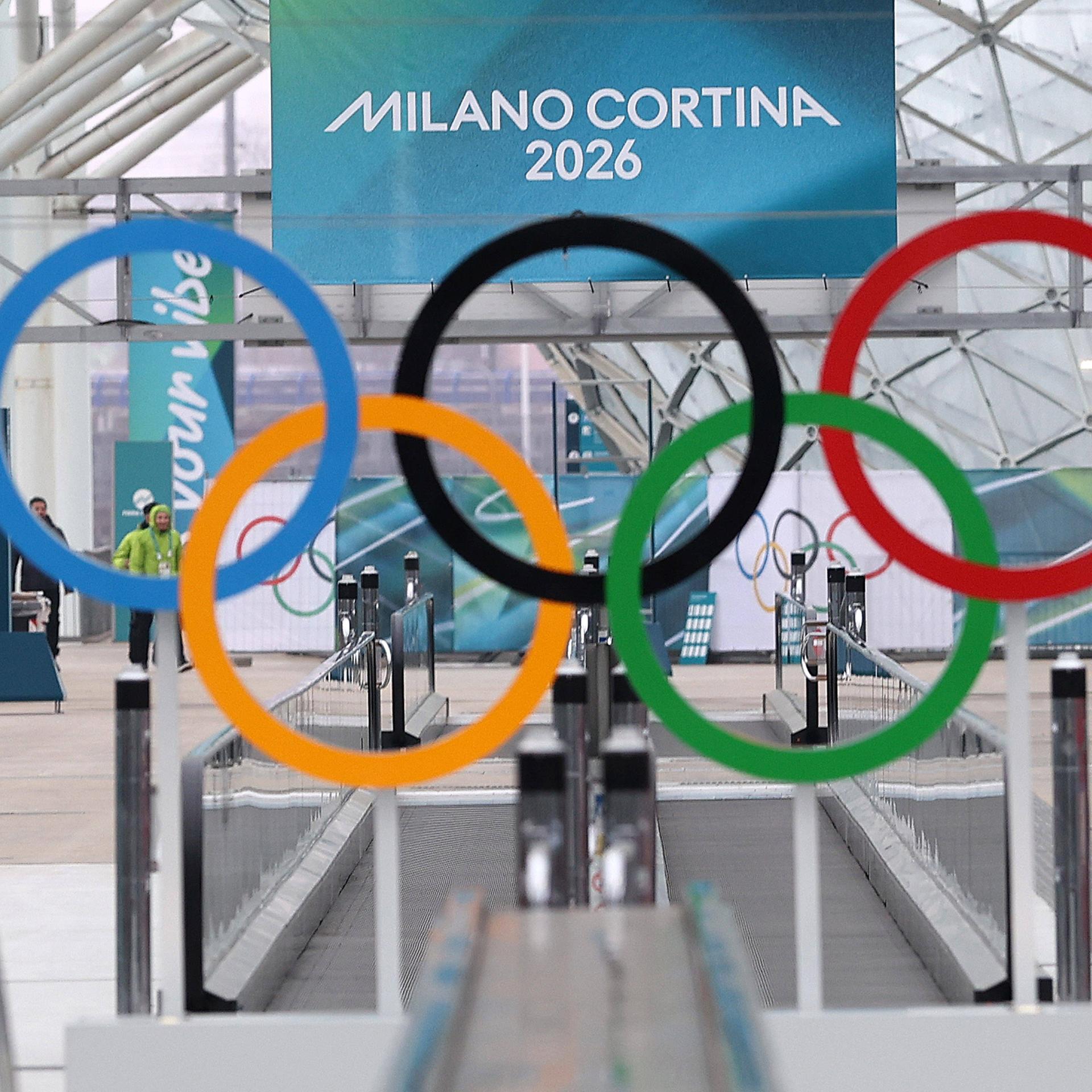 Die olympischen Ringe hängen vor einem Plakat mit der Aufschrift "Milano Cortina 2026".