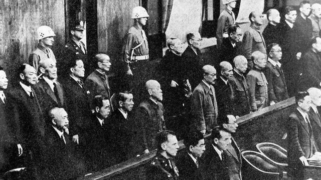 Blick in den Gerichtssaal. Zwischen Holzbänken stehen Männer, teils in Uniformen, teils in Zivil.