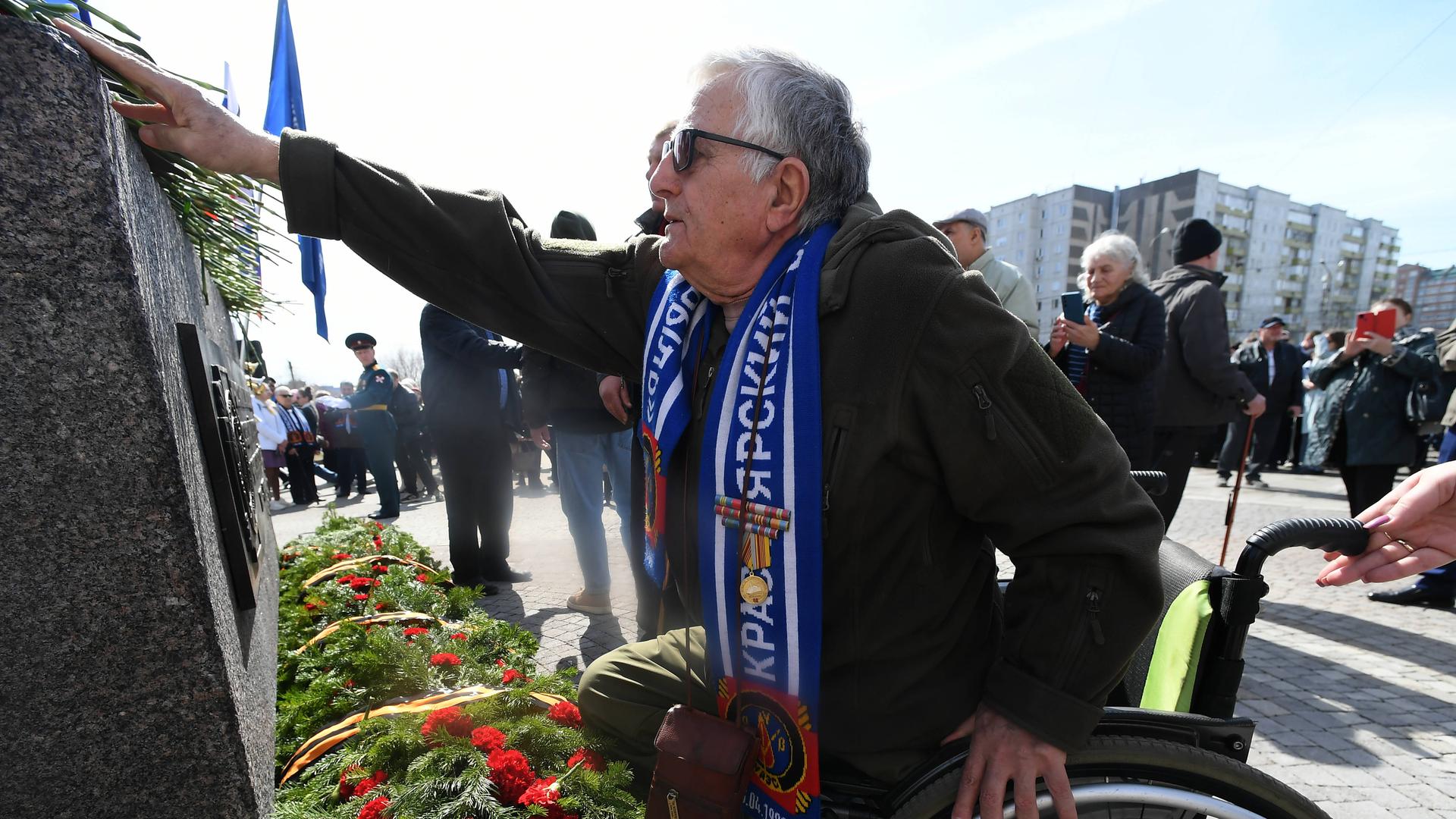 Ein Mann legt Blumen an einem Denkmal nieder.