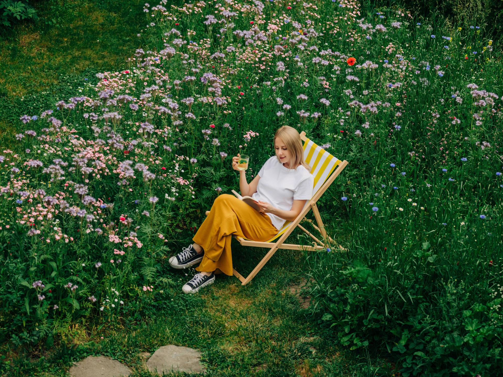Eine Frau sitzt auf einer grünen Wiese und liest in einem Stuhl ein Buch.