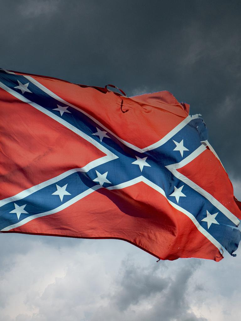 Eine im Wind wehende, zerfledderte "Rebellenflagge", ein weißumrahmtes blaues Schragenkreuz bedeckt mit dreizehn weißen Sternen auf rotem Grund, vor einem grau bewölkten Himmel mit aufziehendem Gewitter. 