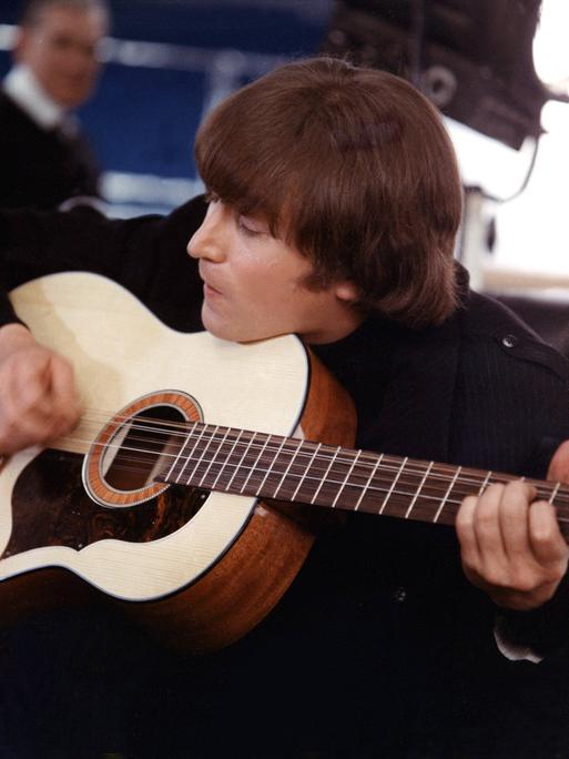 John Lennon sitzt auf einem Sessel und spielt eine Gitarre. 