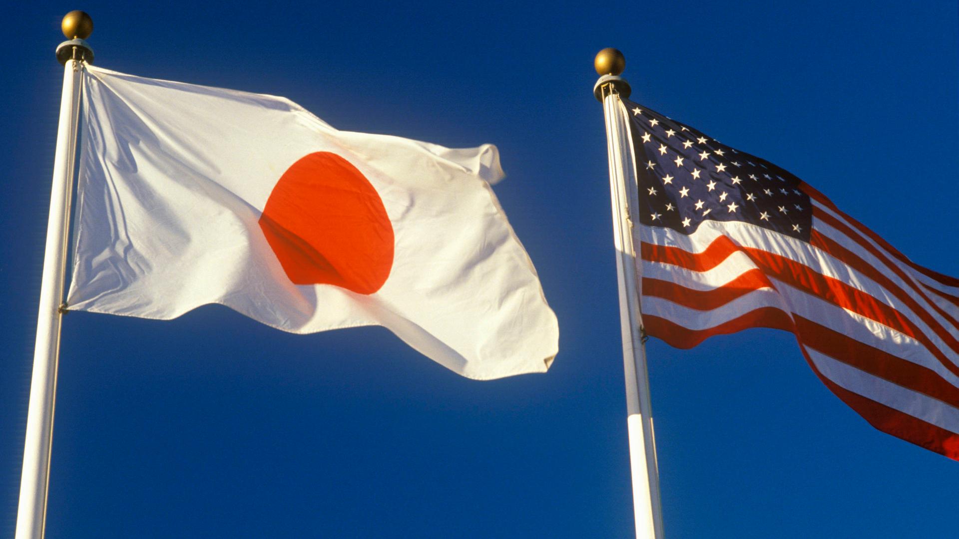 Die amerikanische und die japanische Flagge wehen am blauen Himmel.