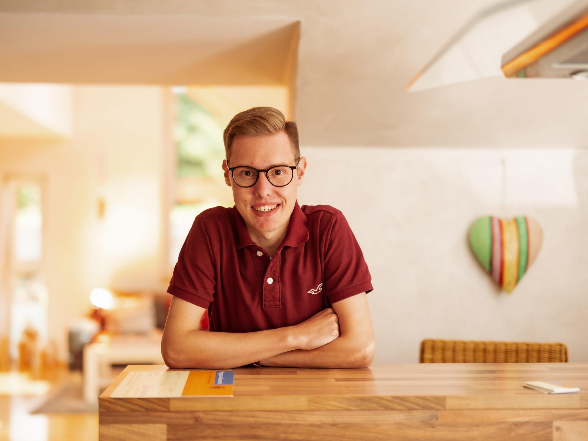 Porträt von Marius Schaefer aus Arnsberg-Oeventrop, der als erster Mensch in Deutschland eine Lebendlungenspende von seinen Eltern erhielt. Er stützt sich mit verschrenkten Armen auf einen Tisch und blickt freundich in die Kamera