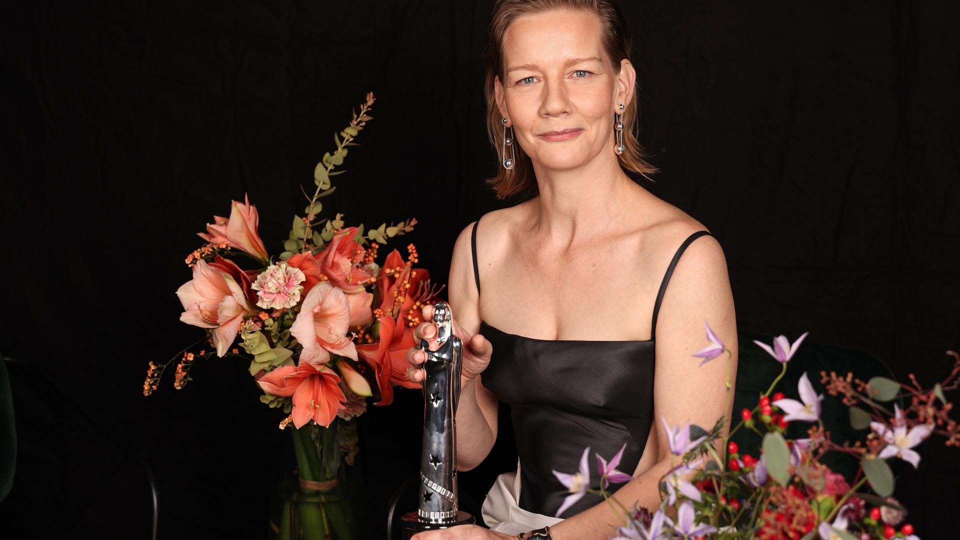 Die Schauspielerin Sandra Hüller hält am 10. Dezember 2023 die Auszeichnung als beste Darstellerin beim Europäischen Filmpreis in der Hand. Sie ist umrahmt von Blumen. 