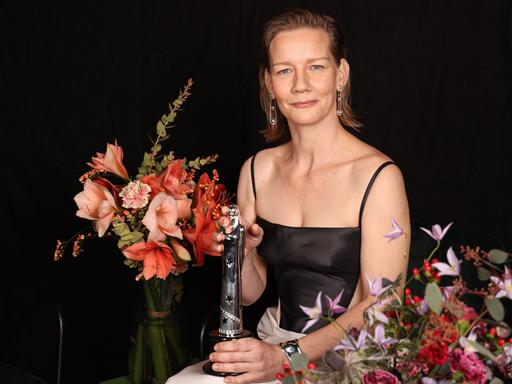Die Schauspielerin Sandra Hüller hält am 10. Dezember 2023 die Auszeichnung als beste Darstellerin beim Europäischen Filmpreis in der Hand. Sie ist umrahmt von Blumen. 