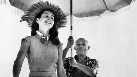 Pablo Picasso läuft am Strand von Cannes hinter Françoise Gilot und hält einen Sonnenschirm in den Händen.
