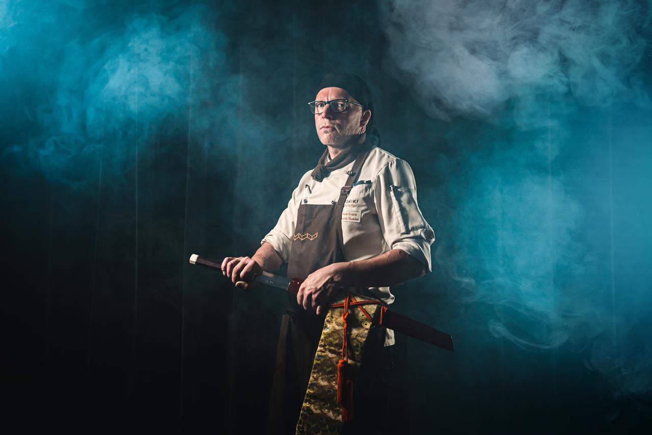 Der Koch Alois Traint steht mit einem großen Messer im Kunstnebel.