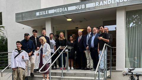 Bewohner und Einwohner auf der Treppe vor dem Eingang. Über der Tür die Aufschrit "Exile-Media-Hub-Brandenburg"