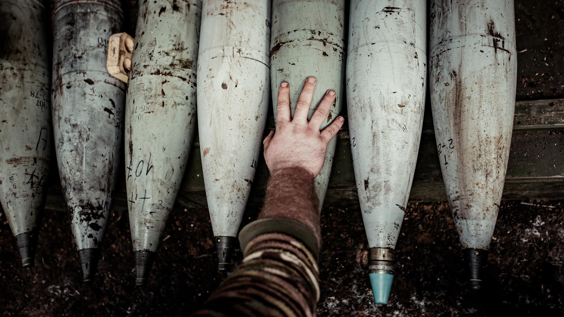Artilleriegranaten und die Hand eines Soldaten.