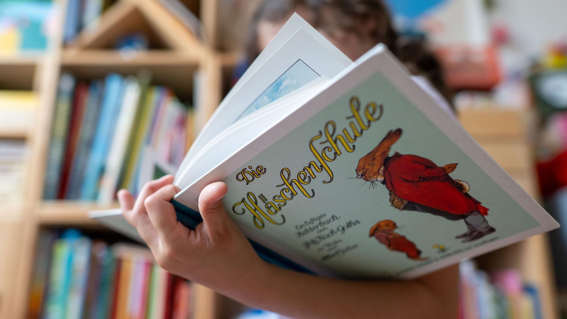 Ein Mädchen hält eine Ausgabe des Kinderbuchs „Die Häschenschule“ (Thienemann-Esslinger Verlag) in ihren Händen. Ein Mädchen hält eine Ausgabe des Kinderbuchs „Die Häschenschule“ (Thienemann-Esslinger Verlag) in ihren Händen.