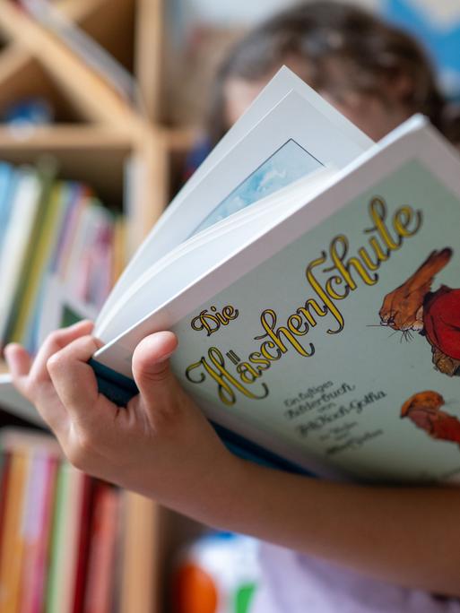 Ein Mädchen hält eine Ausgabe des Kinderbuchs „Die Häschenschule“ (Thienemann-Esslinger Verlag) in ihren Händen.