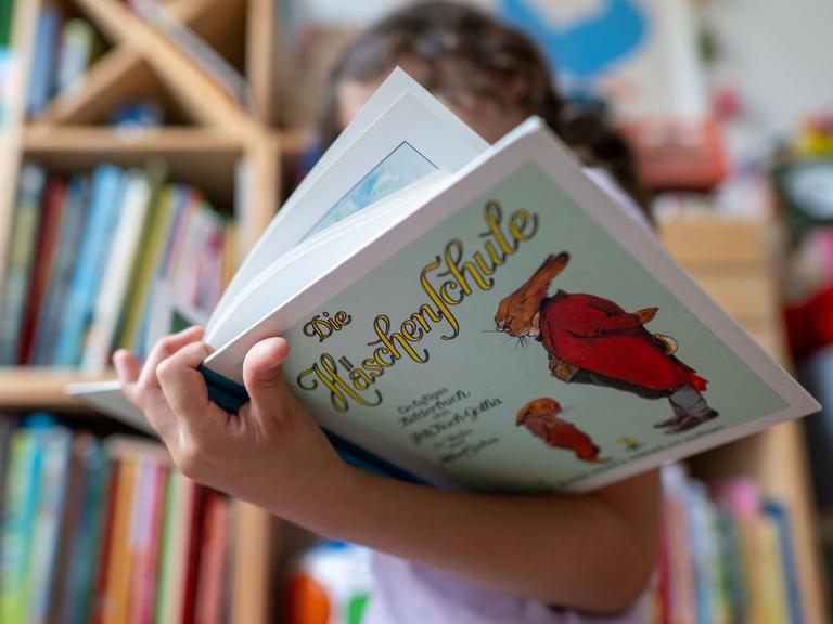 Ein Mädchen hält eine Ausgabe des Kinderbuchs „Die Häschenschule“ (Thienemann-Esslinger Verlag) in ihren Händen.