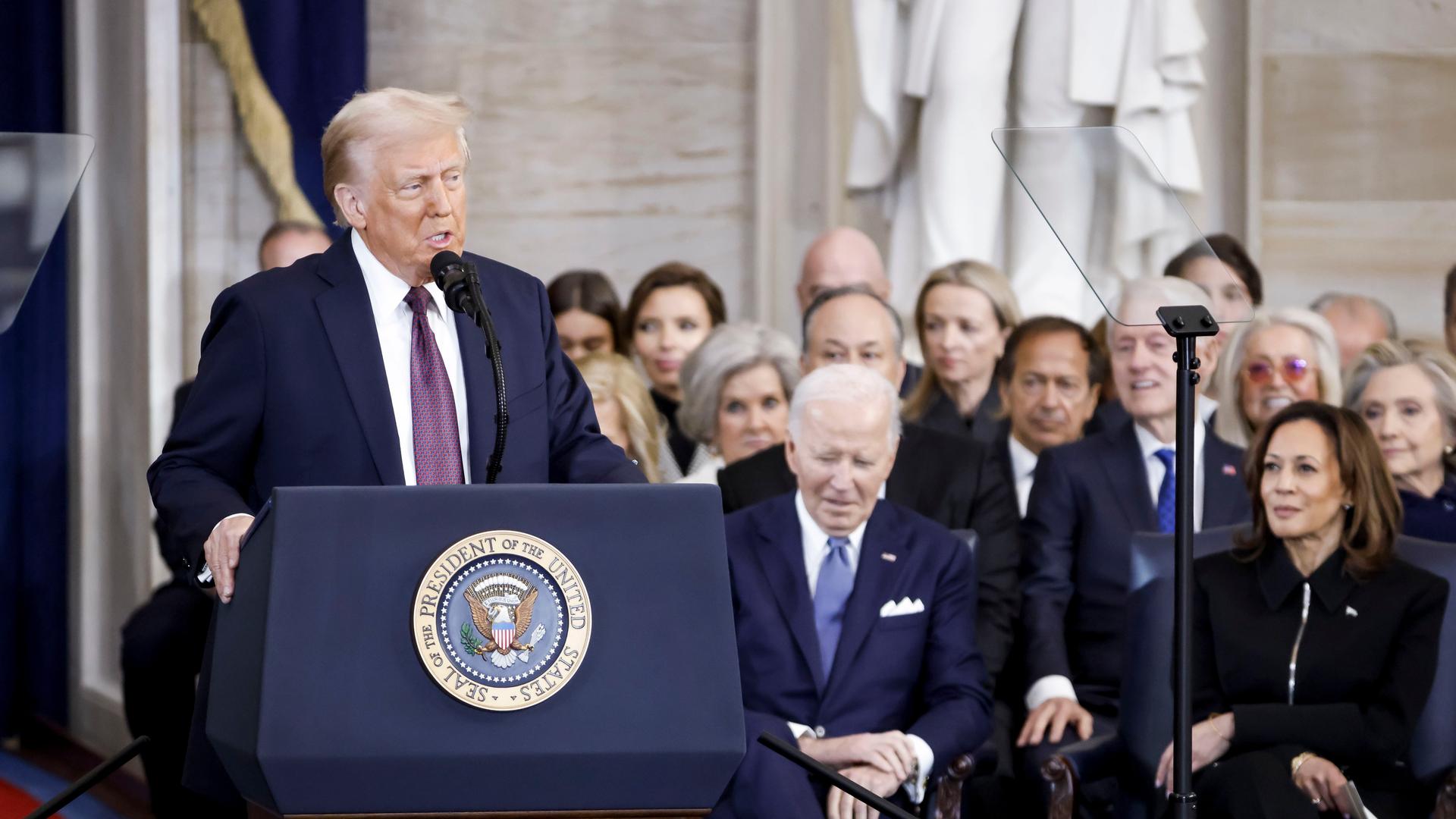 Präsident Donald Trump (l) spricht nach seiner Vereidigung zum Präsidenten der USA in der Rotunde des US-Kapitols in Washington. Der ehemalige Präsident Joe Biden (M) und die ehemalige Vizepräsidentin Kamala Harris sitzen vorne. 